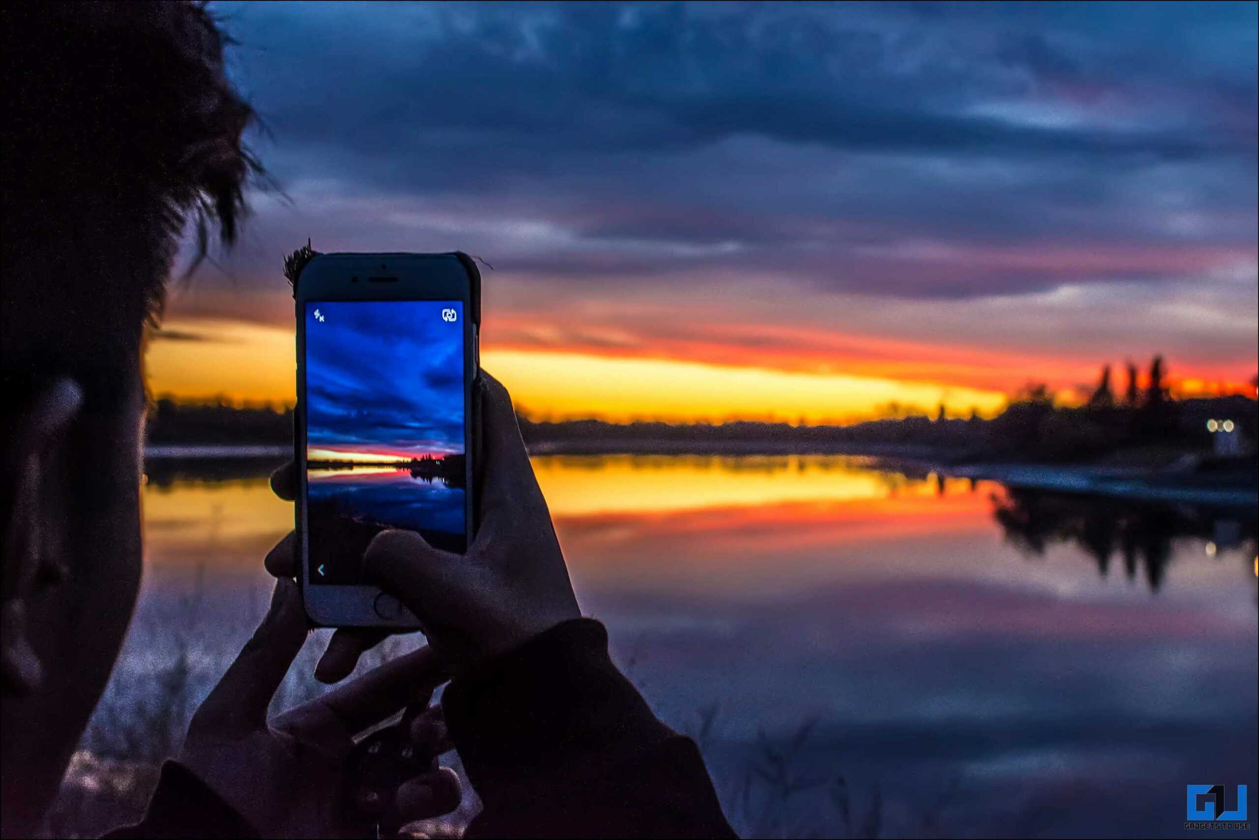 한 남자가 휴대폰으로 호수 근처의 풍경 사진을 클릭하고 있습니다.